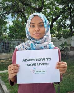 CCN Member, Afeefa, holding a sign which reads 'Adapt Now to Save Lives'